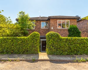 A postwar two-storey brick house behind high hedges