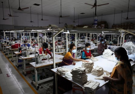 A factory with South Asian women at sewing machines and others at a big table folding clothes