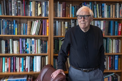 Paul Mullen, a white-haired man with glasses, stands in front of a bookcase
