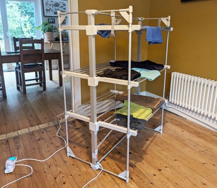 A Dunelm XL 3-tier square heated airer with clothes draped on it in a ochre room with a wooden floor