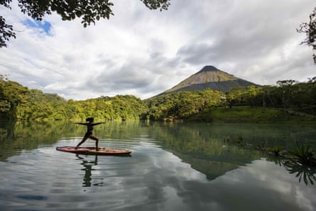 A woman practises yoga on a board in a lagoon in front of a volcano 