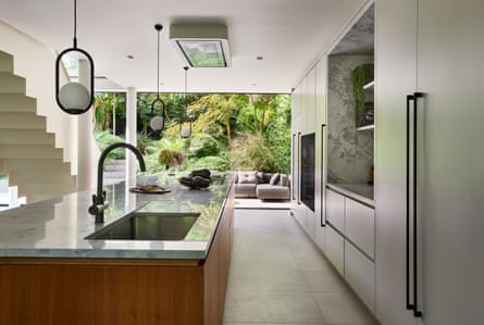 A view from the kitchen out to the garden, featuring a large kitchen island, with steel stairs off to the left and wall of cupboards to the right