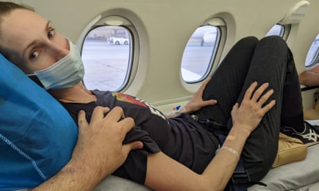 A woman in a medical mask lying on a stretcher on a small plane