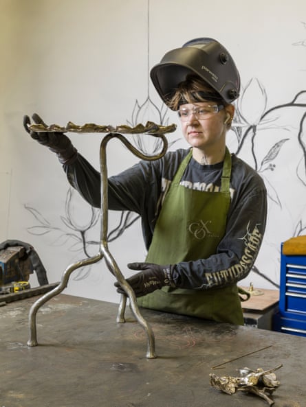 Emerson wearing an apron, gloves and protective headgear, works on a metal item