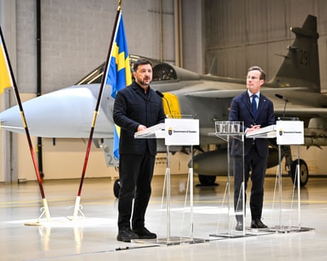 Zelenskyy and Swedish PM Ulf Kristersson speak at podiums in front of military jet in hangar qhxidiqxkiqteinv