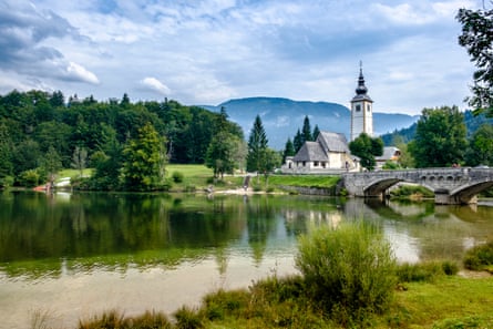 A church and a bridge on a lake with trees and hills in the background
