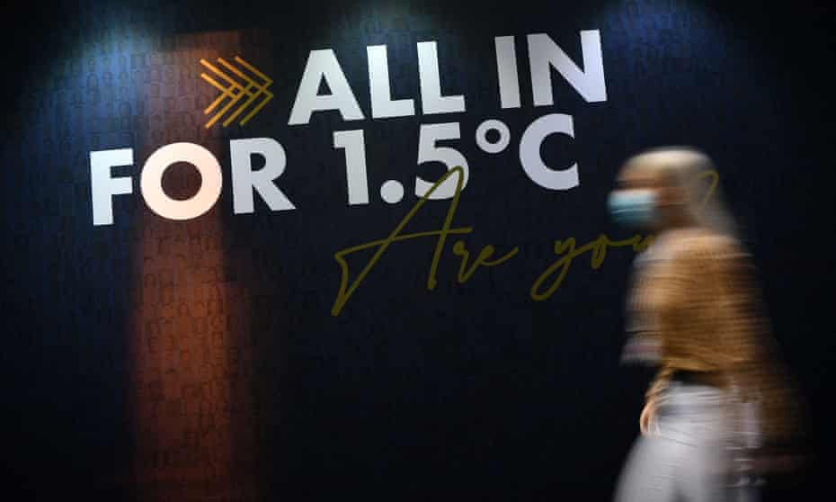 A woman walks past a 'All in for 1.5C' slogan on a wall at Cop26