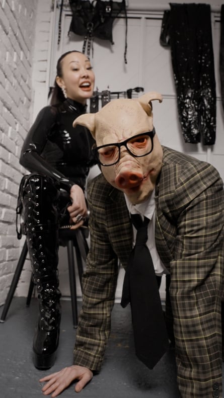 Oh, dressed all in black sits on a chair while a man with a pig’s head kneels in front of her
