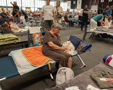 A woman on a camp bed pets a small white dog