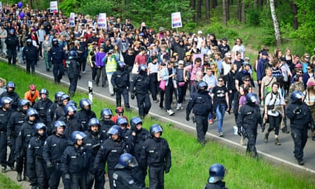 Riot police walk next to environmental campaigners on a path next to a woodland