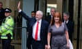Jeremy Corbyn holding up an arm in a wave as he exits a building, with Karie Murphy walking next to him