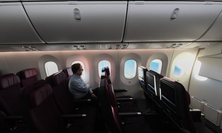 A lone man sitting in an economy class airline seat with sunshine coming in through the windows 