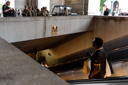 A man descending an escalator looks up at national guard troops standing above the entrance