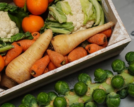 a crate of fresh fruit and vegetables, including carrots, cauliflower, parsnips, brussel sprouts, apples and oranges.