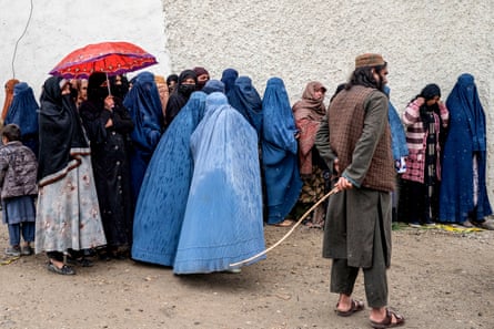 Taliban security personnel stand guard women wait in a queue for food supplies donated during Ramadan, Kabul, March 2025.