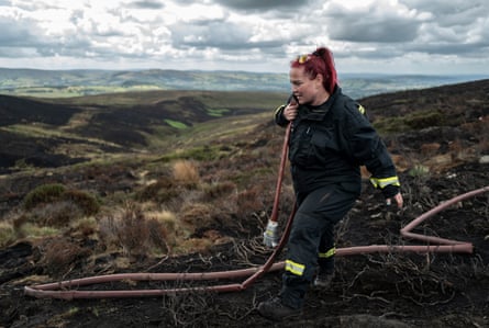 A firefighter carries a hose amid burned moorland in Glossop, England, on 6 August.