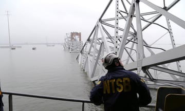 man in a hard hat peers over river at collapsed steel bridge
