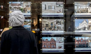 A woman looking at houses for sale in the window of an estate agents in London.