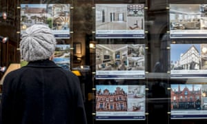 A woman looking at houses for sale in the window of an estate agents in London. 