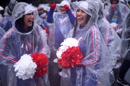 US cheerleaders holding pom-poms laugh while wearing plastic ponchos