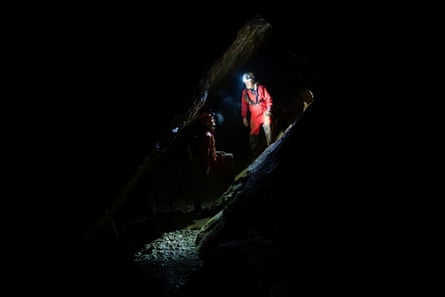 Two people in the dark of a cave, visible only by the light from head torches.