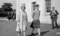 Queen Elizabeth II touring the grounds outside a stone school building with her son Charles in sweater and kilt