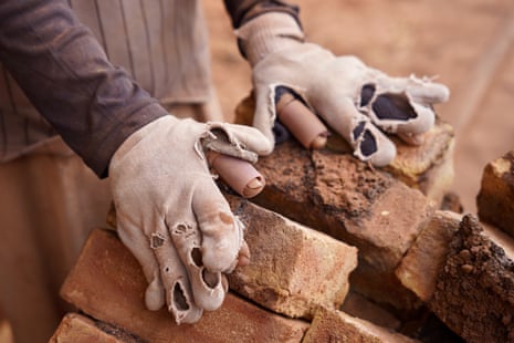 Hands in old gloves full of holes and falling apart place bricks on a stack.