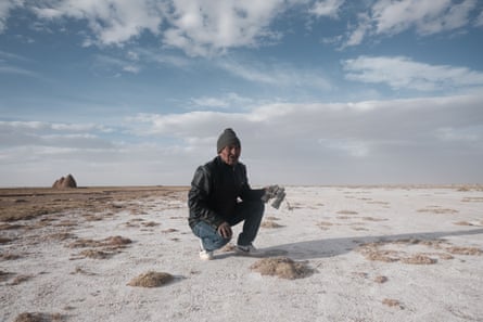 A man crouching on the ground, which is dusted with salt.
