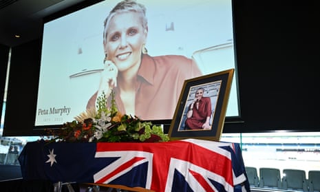 Flowers and a frame with a photo Peta Murphy inside sit on top of a coffin draped with an Australian flag. A large screen showing another photo of Peta Murphy hangs behind the coffin