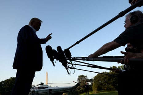 A man in shadow speaks before a bank of microphones.