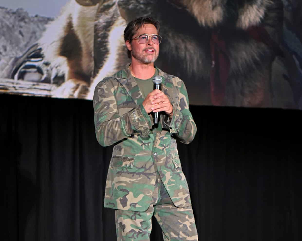 Brad Pitt in a camo suit holding a microphone