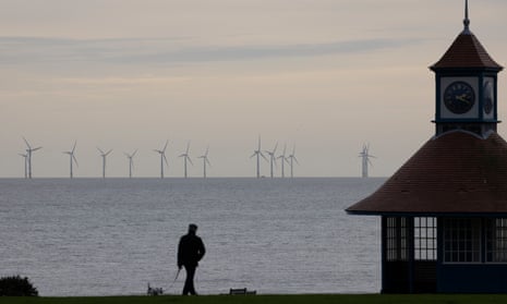 Man walking dog with wind turbines in distance off the coast of Frinton-on-Sea in England.