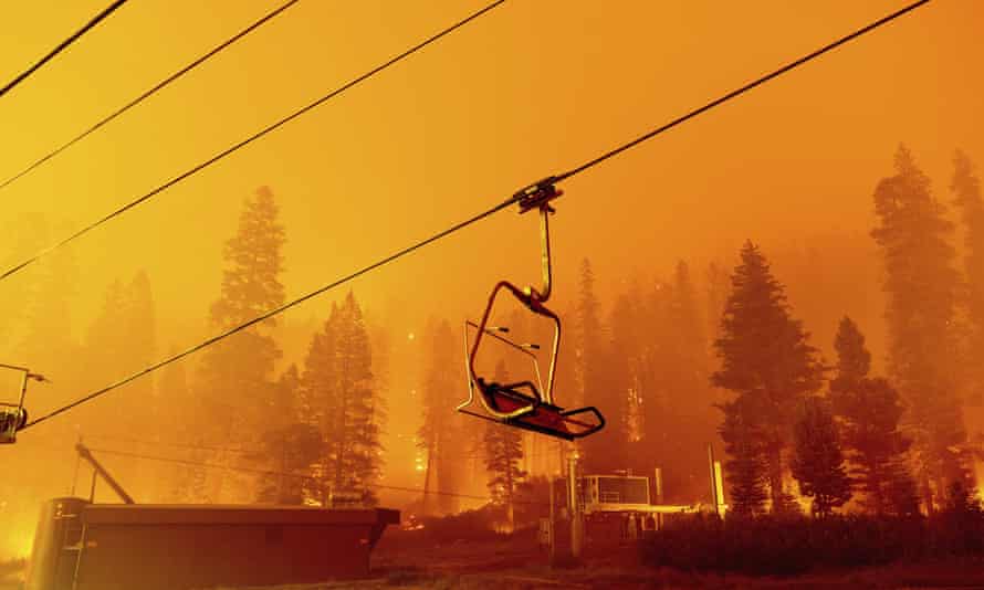 An empty ski lift is seen as a raging wildfire fills the area with smoke and turns everything orange. 