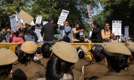 People stand on police barricades as they hold placards and shout slogans during a protest in Dehli