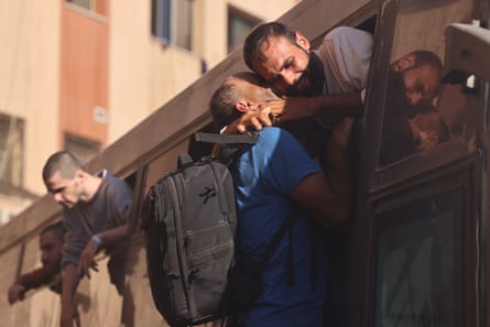 A man embraces a prisoner through the window of the bus, both seem close to tears