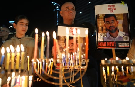 People stand behind burning candles holding posters of Ran Gvili