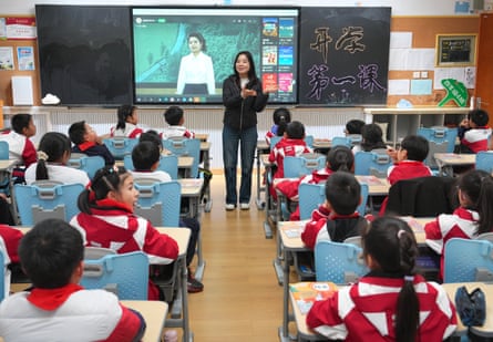 School students face their teacher in a classroom with a screen on the back wall