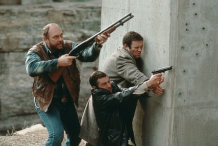 three men hide behind wall, two of them holding guns