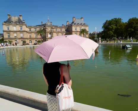 A tourist stands in the shade of an umbrella in the Jardin du Luxembourg, the garden of the French Senate in Paris.