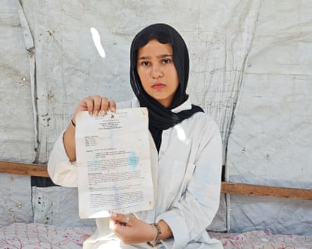 Layan al-Jbour, 15, in a makeshift shelter, holds up a cardiology report from a hospital.