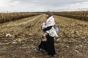 A woman carries her child, as refugees walk along a dirt road towards the border between Serbia and Croatia, near the town of Sid.