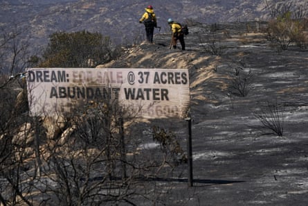 Fire crews work on dry terrain over a sign that says ‘dream: for sale @ 37 acres, abundant water’