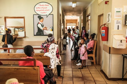 People wait on benches and stand in the corridor of a clinic