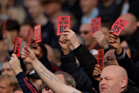In the 15th minute of an FA cup game against Leeds, West Ham fans hold up red cards with “No BS” on them aimed at owner David Sullivan and vice-chair Karren Brady.
