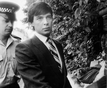 A black and white image of a man in a suit and tie followed closely by a policeman