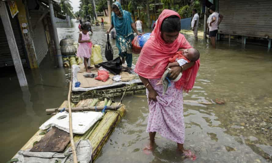 A woman carrying a child wades through flood water in Barpeta