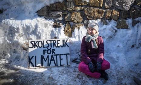 Greta Thunberg sits next to a placard reading “school strike for climate”