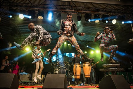 Three men on a stage leap high in the air in front of a drum kit