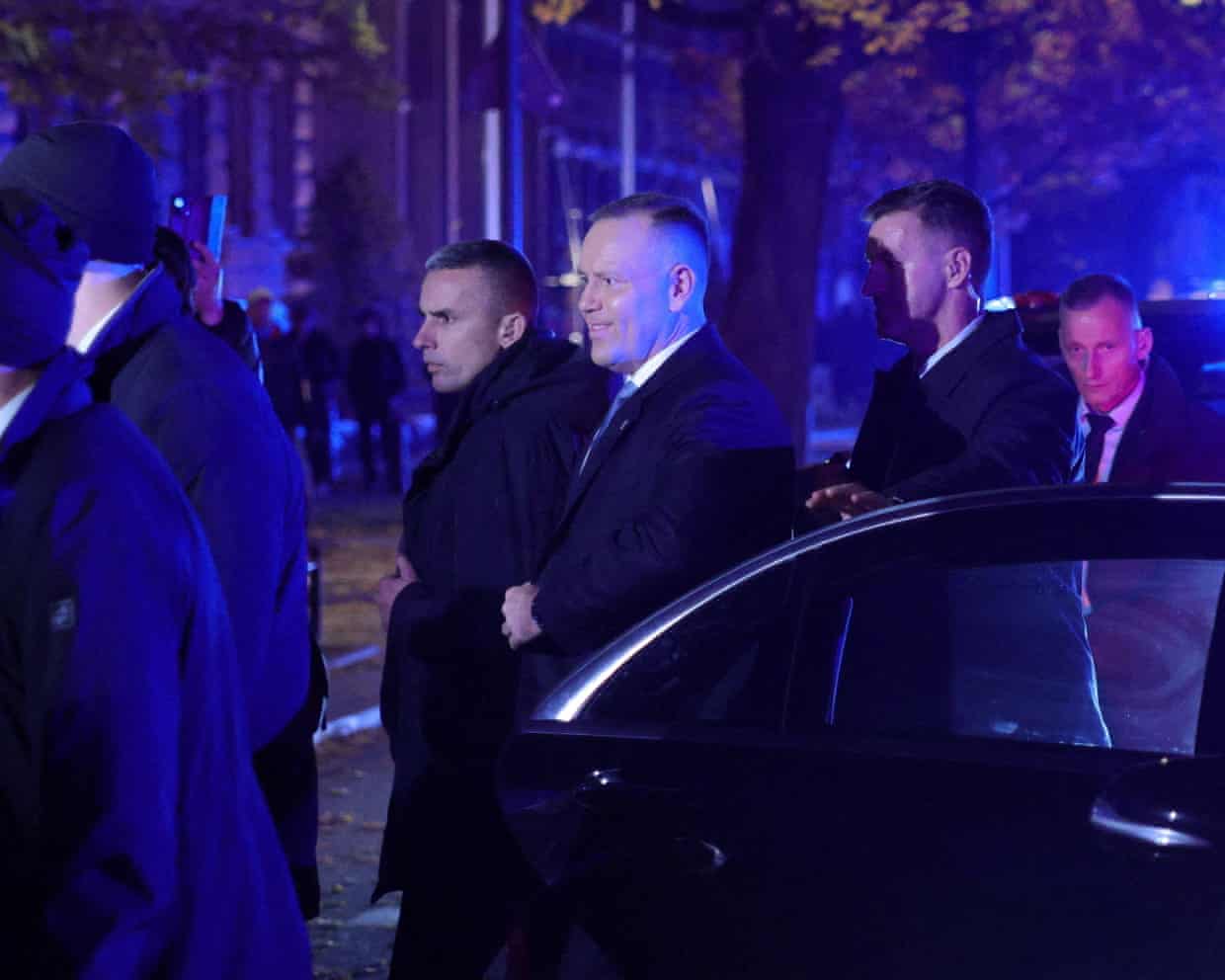 Polish President Karol Nawrocki, surrounded by security at night, walks out from his car