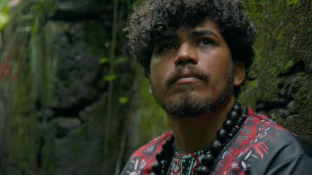 Portrait of a young man of mixed heritage wearing beads by some mossy rock